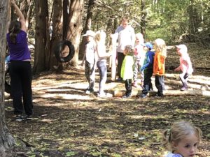 older children helping younger children use tire swing in forest